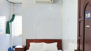A bedroom with a bed, a wooden nightstand, a wall-mounted air conditioner, and a door with a room number. - Gia Tu Hotel (Bien Hoa)