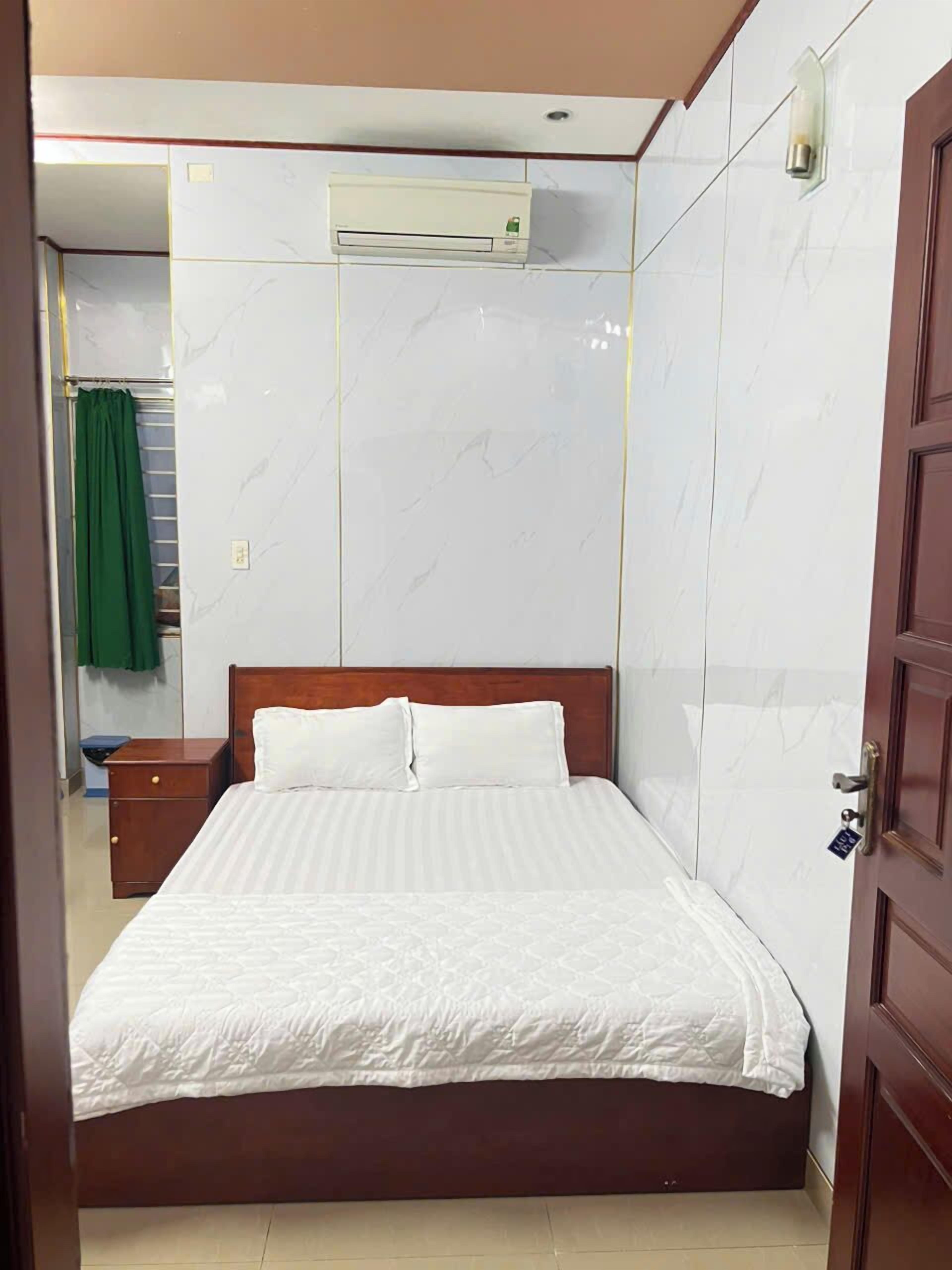 A bedroom with a bed, a wooden nightstand, a green curtain, and an air conditioning unit on the wall.