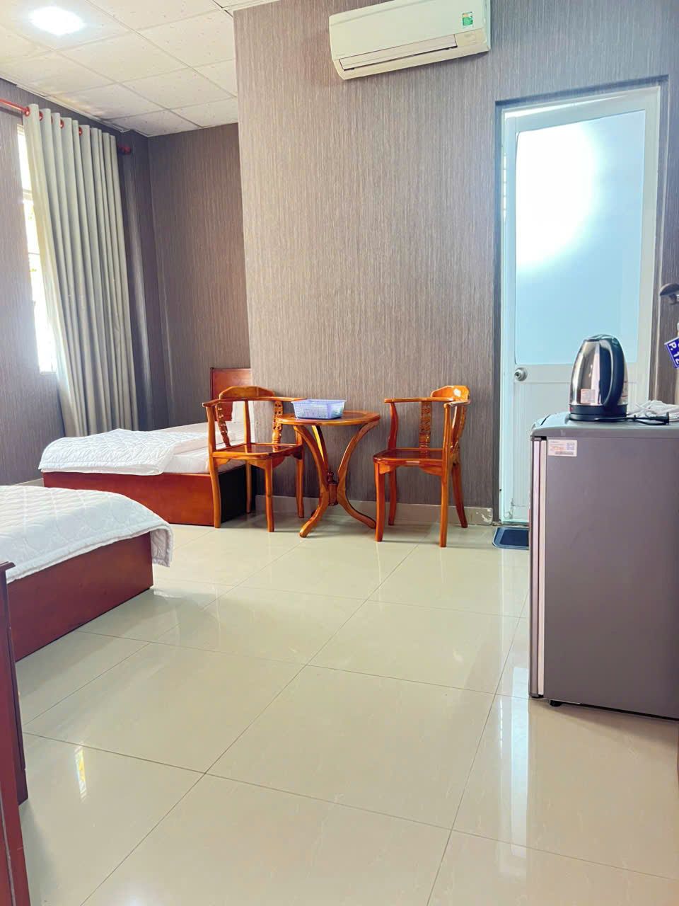 Quarto de hotel com duas camas, uma escrivaninha com cadeiras, chaleira e ar condicionado.