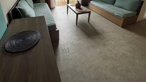 Un salon moderne avec un canapé, une petite table et une table basse. Une porte-fenêtre coulissante donne accès à un espace extérieur aménagé avec des chaises et une table.