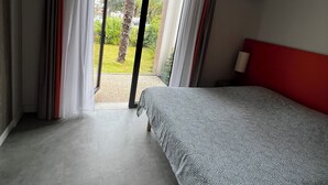Une chambre à coucher avec un lit, une tête de lit rouge et une vue sur un jardin, accessible par une porte coulissante.