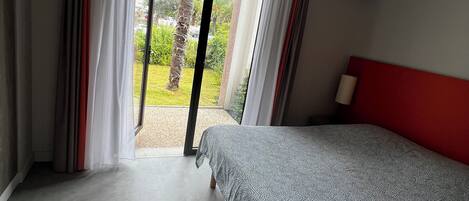 A bedroom with a bed, a red headboard, and a view of a garden through a sliding door.