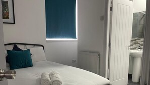 Una camera da letto con un letto, una finestra, un termosifone e un bagno visibile attraverso una porta aperta.