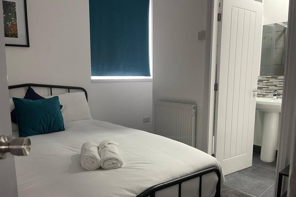 A bedroom with a bed, a window, a radiator, and a bathroom visible through an open door.