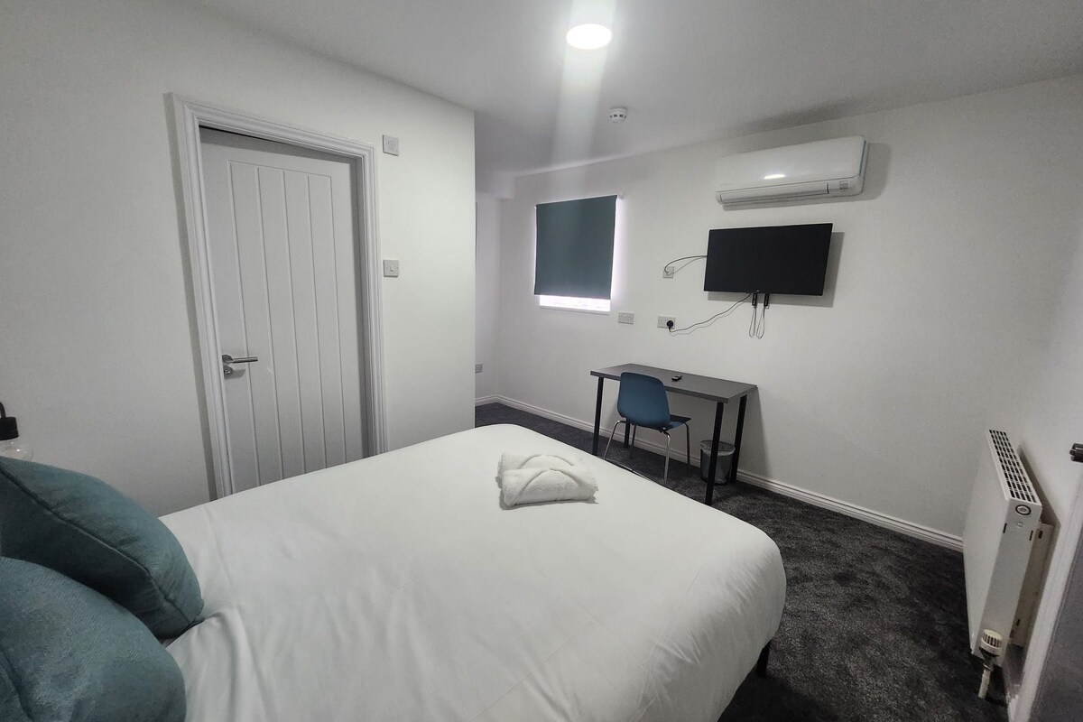 Ein Hotelzimmer mit Bett, Schreibtisch, Stuhl, Fernseher und Klimaanlage.