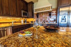 A kitchen with granite countertops, a wine glass, a bowl of fruit, and wooden cabinets. - Hacienda  beachfront  luxury condo! (Cabo San Lucas)