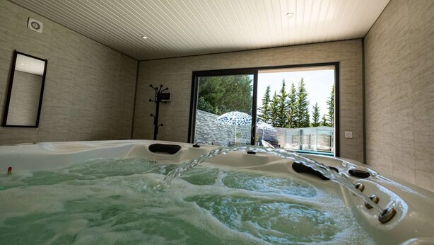 Ett modernt spa-rum med ett bubbelbad, ett stort fönster med utsikt över träd och ett tak med infälld belysning.