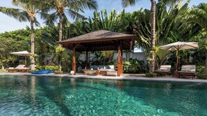 Piscina límpida com espreguiçadeiras e um gazebo rodeado por vegetação tropical.