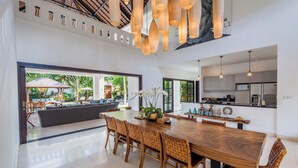 Uma sala de estar ampla com uma grande mesa de jantar de madeira, cadeiras de vime e vista para a área da piscina.