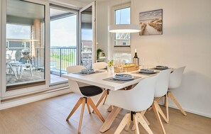 A dining area with a white table set for four, wooden chairs, a glass-top table, and a painting on the wall. - Cozy apartment in Olpenitz with sauna (Olpenitz)