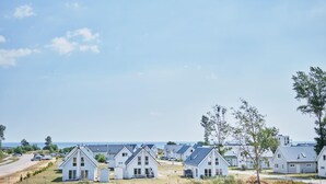 A row of white, single-story houses with gabled roofs, arranged in a row along a road with a view of the sea in the background.