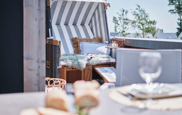 A sun lounger with striped cushions and a fluffy throw, a wicker chair, and a table with a glass of wine. - Cozy apartment in Olpenitz with sauna (Olpenitz)