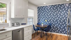 A kitchen with white cabinets, a dishwasher, a toaster, and a dining table with blue chairs. - Renovated Capital Heights Home (Baton Rouge)