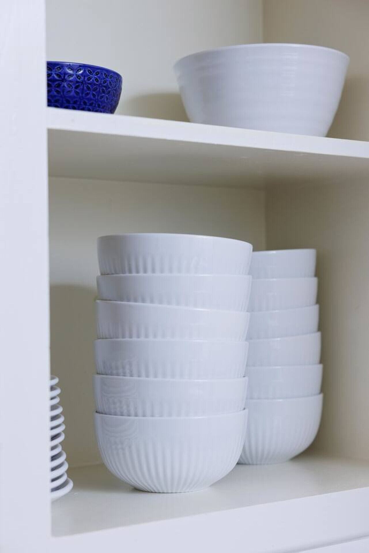 A white shelf with stacked white bowls and a single blue bowl.