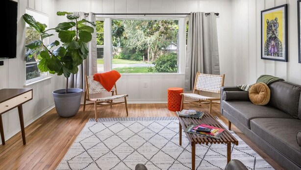 A living room with a large window, a potted plant, a sofa, a coffee table, and a TV. - Renovated Capital Heights Home (Baton Rouge)