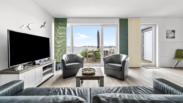 Una sala de estar moderna con un televisor de pantalla plana grande, sofás de cuero y un balcón con mobiliario exterior.
