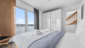 Un dormitorio moderno con una cama grande, vistas al agua y un balcón.