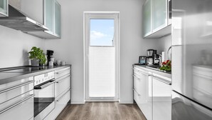 Una cocina moderna con electrodomésticos de acero inoxidable, piso de madera y vistas a través de una puerta.