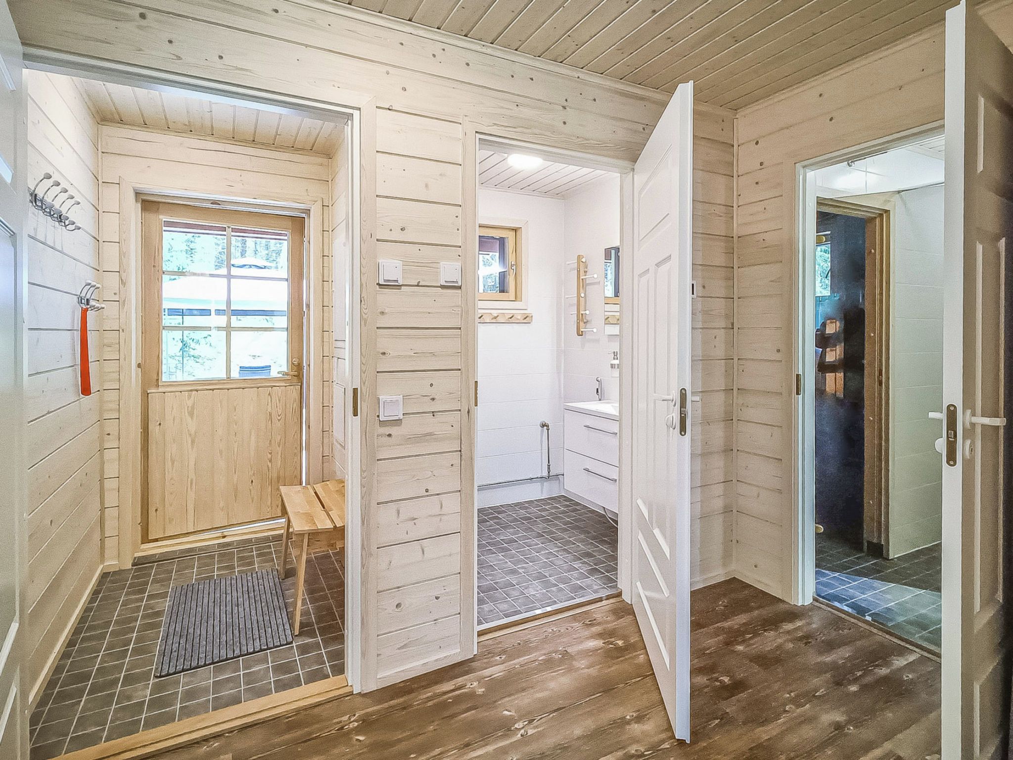 Un interior de madera con una puerta que da a un baño, un pequeño banco de madera y un suelo de baldosas.