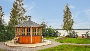 Un gazebo in legno con un vialetto sterrato che vi conduce, circondato da erba e alberi.