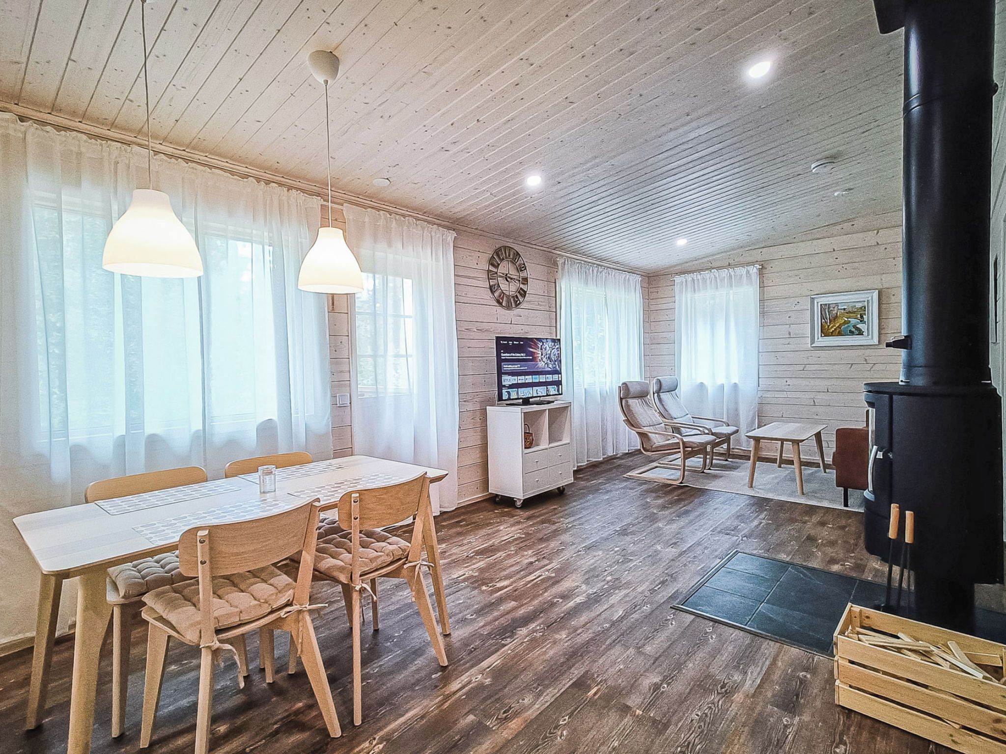 Una sala de estar acogedora con piso de madera, una mesa de comedor con sillas, un sofá, un televisor y una chimenea.