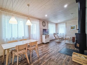 A cozy living room with a wooden floor, a dining table with chairs, a sofa, a TV, and a fireplace.