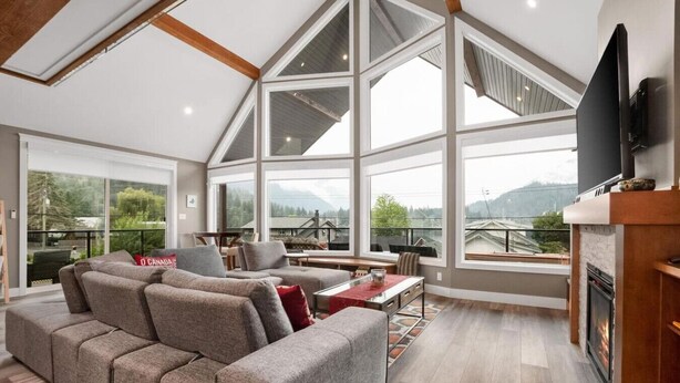 Un salón amplio con un sofá seccional grande, una chimenea y un ventanal con vistas al exterior.