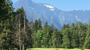 Un campo de golf con montañas al fondo, rodeado de árboles.