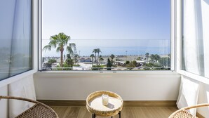 Un balcon donnant sur la plage, une chaise en osier et une petite table avec une bougie.
