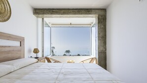Une chambre avec un grand lit, une vue sur la mer et une petite table avec des chaises.