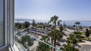 Un parking avec des voitures, des palmiers et une vue sur l’océan.