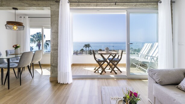 Un salon moderne avec une porte vitrée donnant sur un balcon qui offre une vue sur la mer.