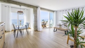 Un salon moderne avec un coin repas, de grandes fenêtres et une vue sur la mer.