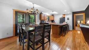 A modern kitchen with wooden cabinets, a dining area with a large table and chairs, and a cozy seating area with a sofa. - Rustic Cabin with 4 Master Suites by SDC! (Branson West)