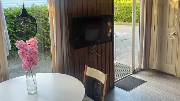 Una habitación con una mesa redonda, sillas, un televisor montado en la pared y vistas al exterior a zonas verdes.