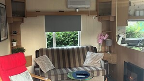 Un espacio habitable pequeño con un sofá, una silla roja, una mesita, una chimenea y un ventanal con vistas a zonas verdes.