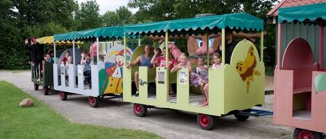 A colorful children's train with cartoon characters, moving along a paved path in a park.