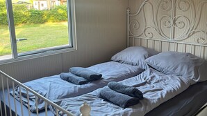 Una cama individual con estructura metálica, ropa de cama blanca y vistas a un jardín por una ventana.