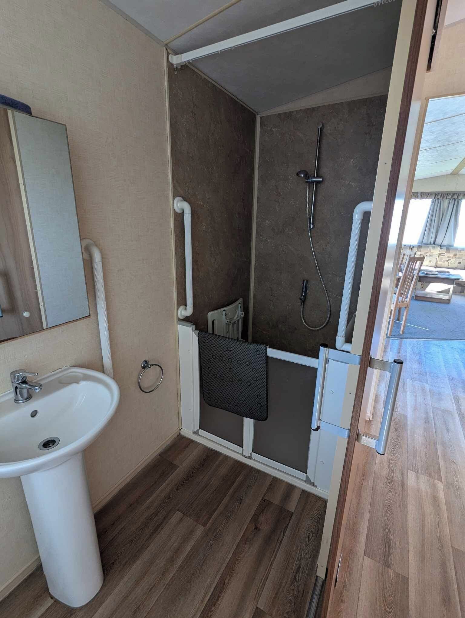 A compact bathroom with a sink, mirror, shower, and towel rack.