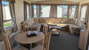 A caravan interior with a sofa set, a round table, and chairs. - ml Accessible Caravan in Ingoldmells Skegness (Skegness)