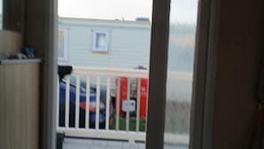 A room with a sliding glass door leading to a balcony. The balcony has a white railing and a small window. There is a mat at the door's entrance. - ml Accessible Caravan in Ingoldmells Skegness (Skegness)