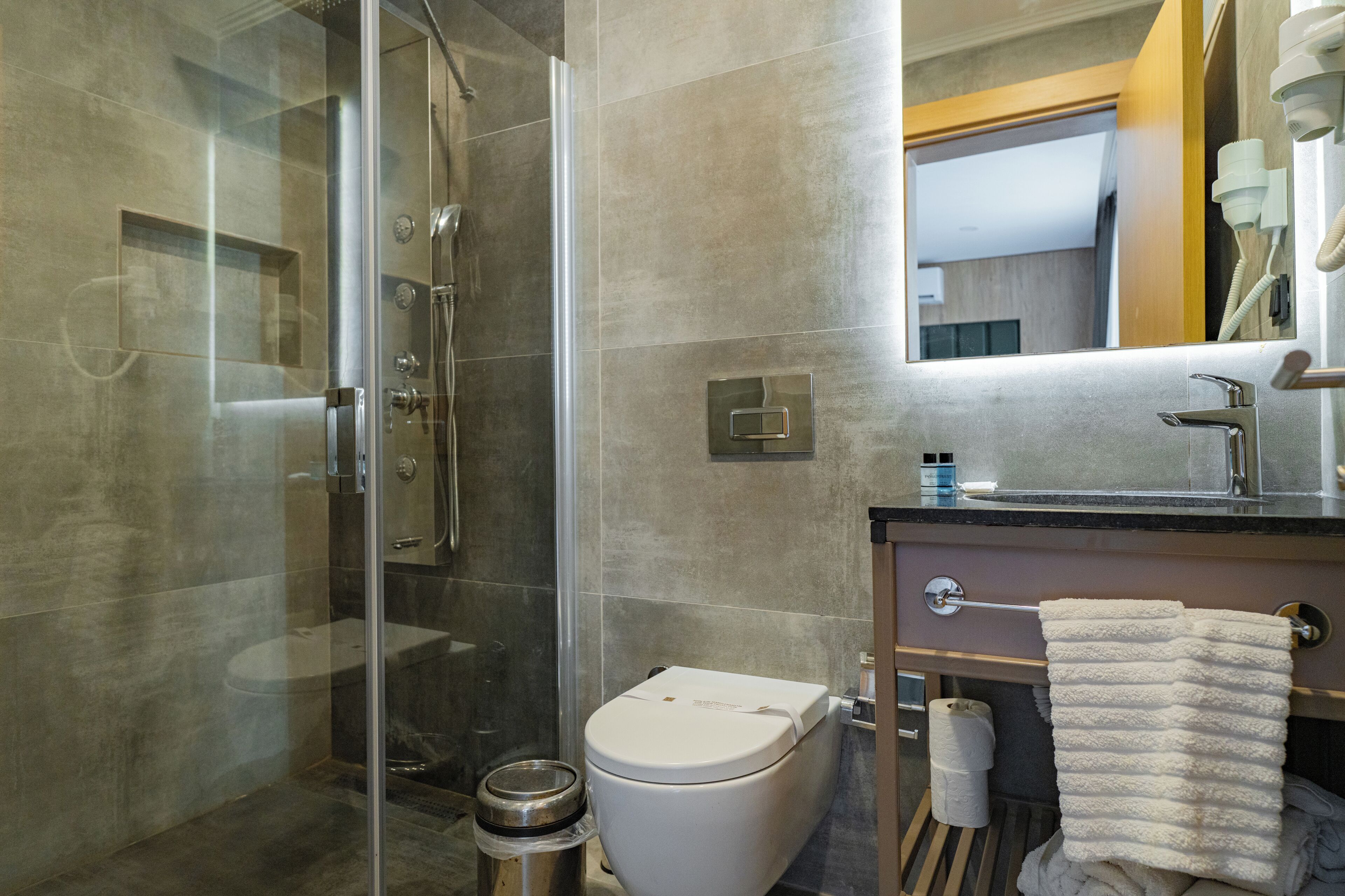 Un baño moderno con ducha envuelta en vidrio, inodoro, lavamanos con toallero y espejo.
