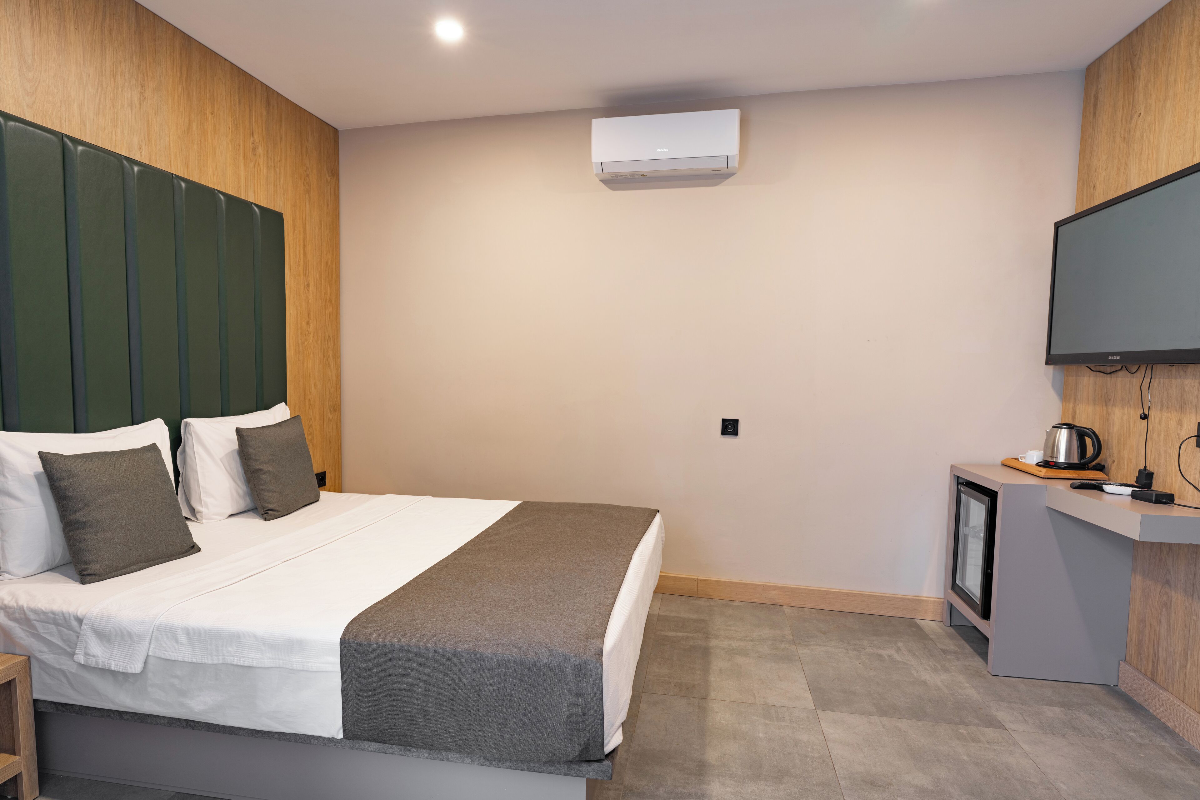 Une chambre d’hôtel moderne équipée d’un lit, d’une télévision, d’une petite kitchenette et d’un système de climatisation intégré.