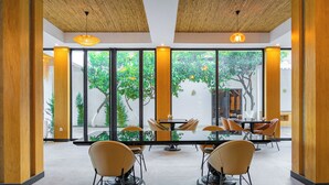 A modern indoor dining area with large windows, wooden pillars, and a central table with chairs. - Perast Garden Hotel (Kemer)