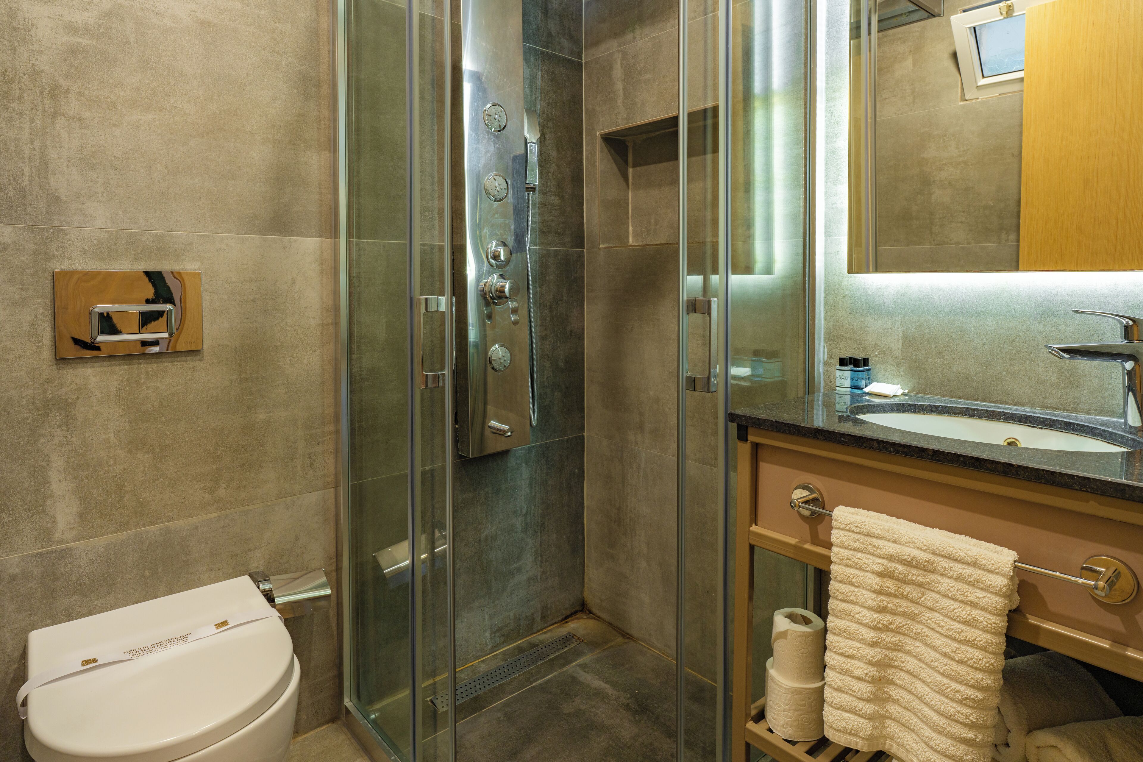 Un baño moderno con ducha envuelta en vidrio, inodoro, lavamanos con espejo y barra para toallas.