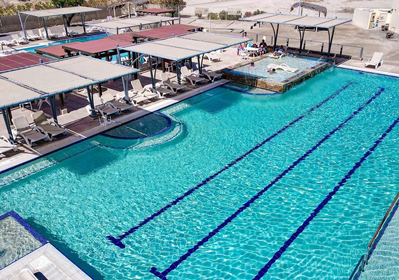 Une piscine avec plusieurs couloirs de nage, des chaises longues et des zones ombragées.