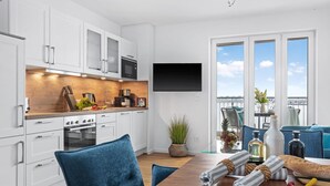 Eine moderne Küche mit weißen Schränken, einer Holz Arbeitsplatte und einem eingebauten Backofen. Ein Flachbildfernseher ist an der Wand oberhalb der Arbeitsfläche angebracht.