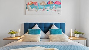 Ein Schlafzimmer mit einem großen Bett, zwei Nachttischen und einem Strandbild über dem Bett.
