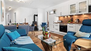 Ein modernes Wohnzimmer mit Sofa, Couchtisch und Küchenzeile mit Schränken und Geräten.