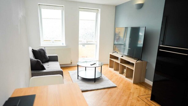 A modern living room with a sofa, a coffee table, a TV on a stand, and a refrigerator. - One Bedroom Flat in Gravesend Kent (Gravesend)